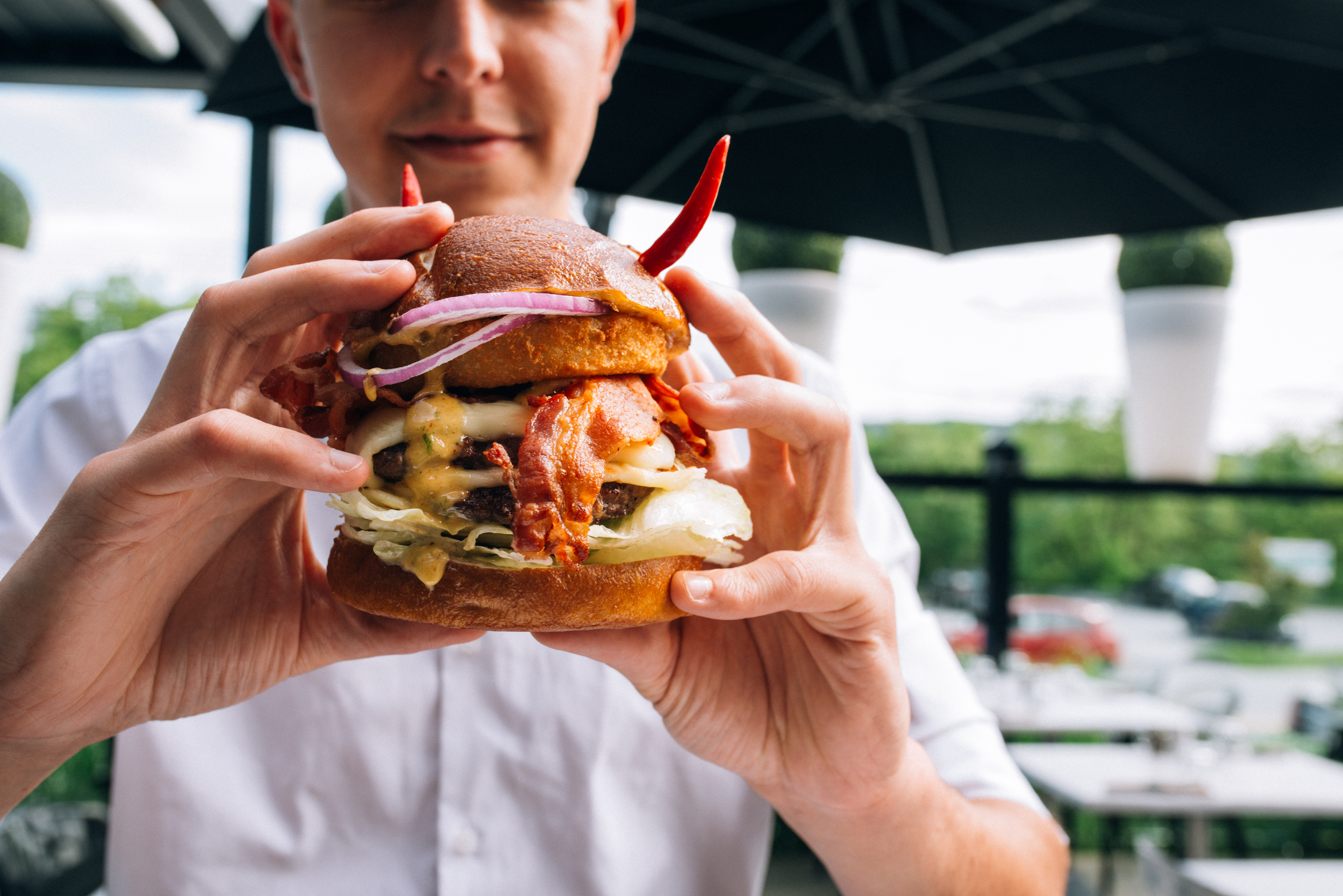 Un client du OMG Resto sur la terrasse s'apprête à prendre un boucher de son burger